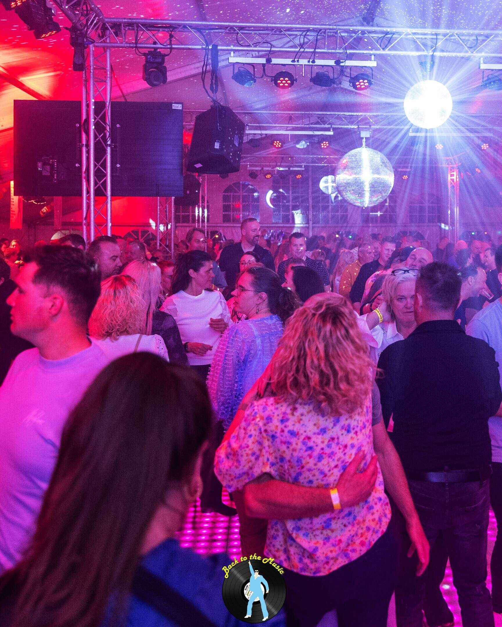 De dansvloer van Back to the Music bruist van energie, met mirrorballen, lasers en een volle tent vol feestvierders.